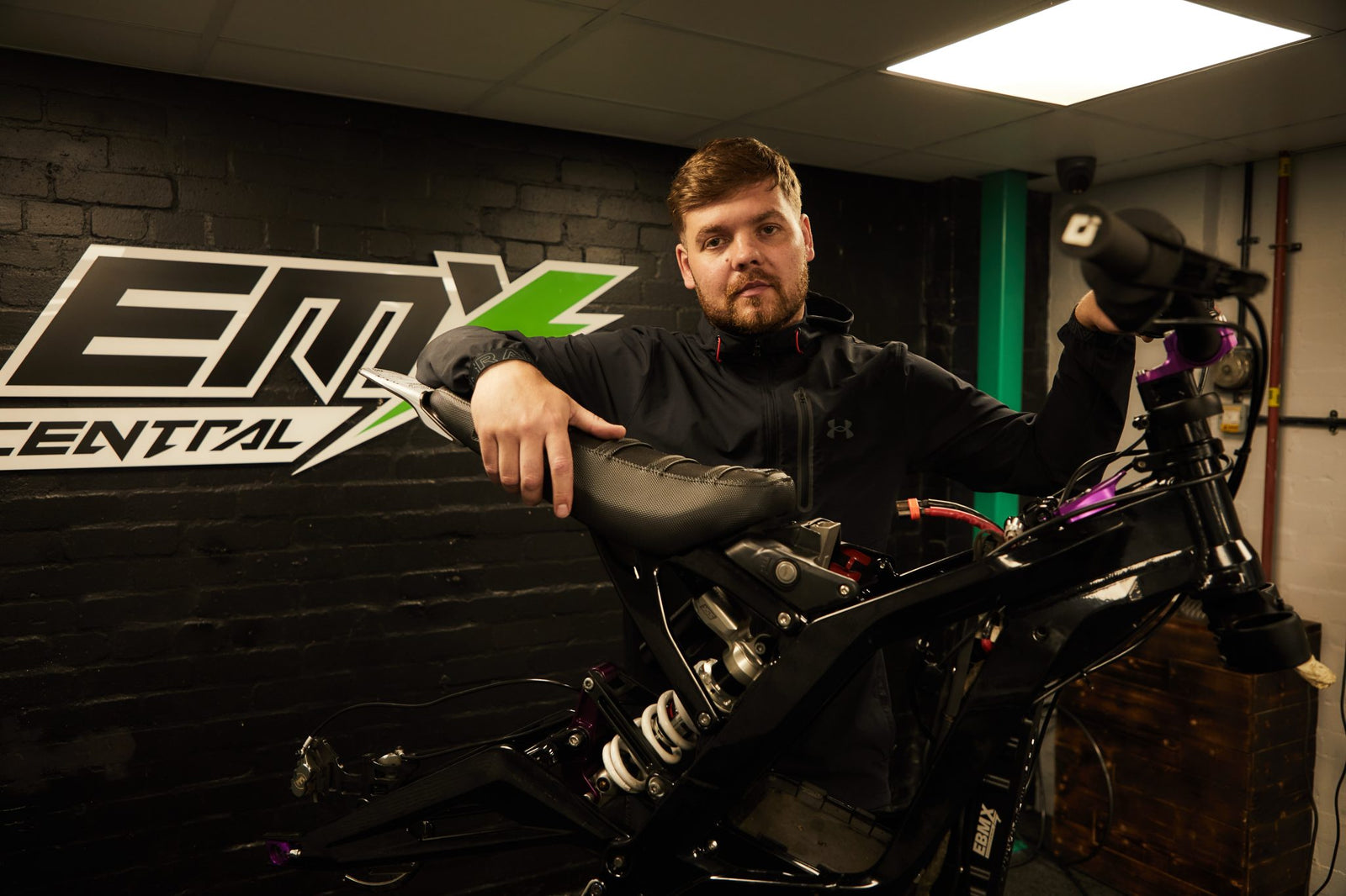 Company Director Jake, stood in front of EMX Central logo with a surron light bee