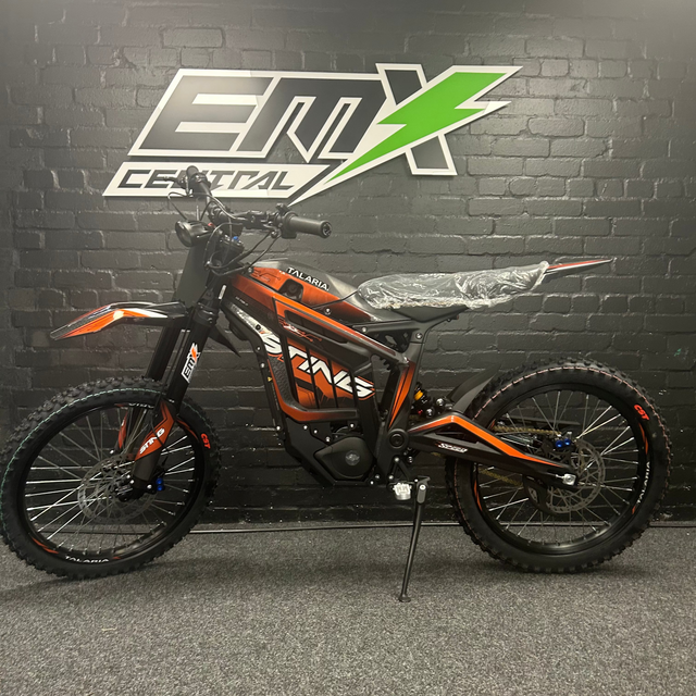 Orange and black dirt bike in front of a black brick wall with a logo.