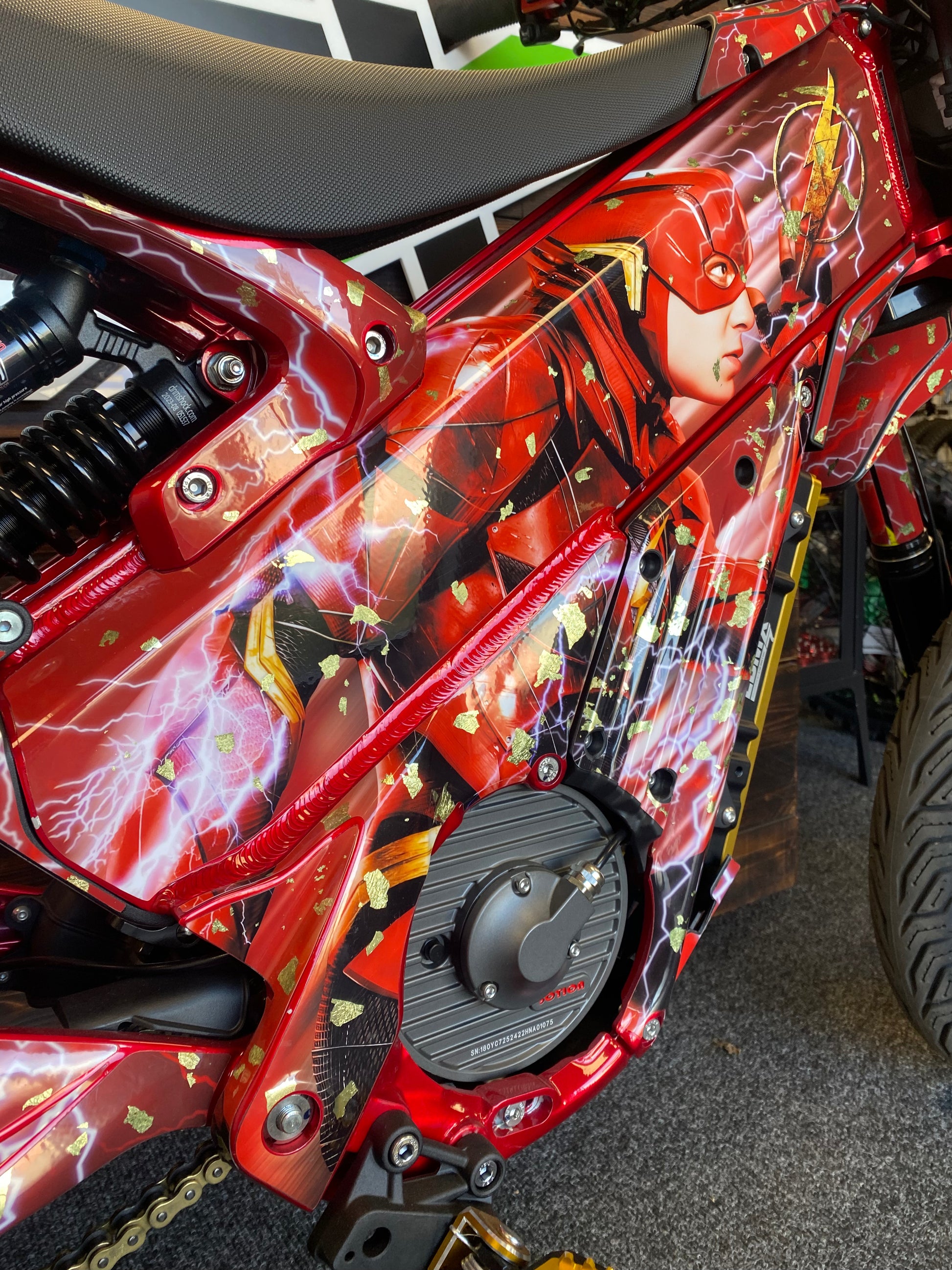Close-up of a red motorcycle or scooter body panel featuring a detailed Flash comic-style graphic with lightning effects, shown in a workshop setting.