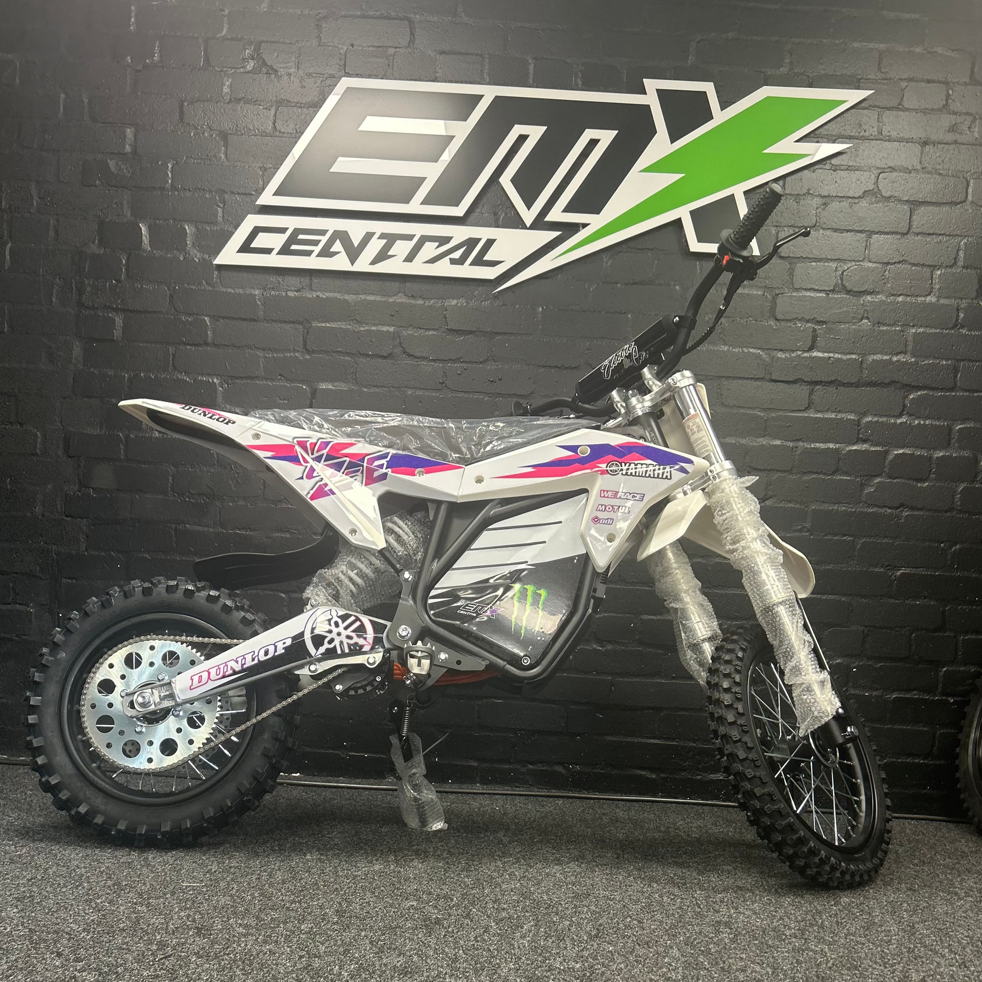 Small dirt bike in front of a black wall with 'EMX Central' logo