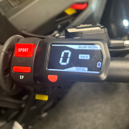 Close-up of a motorcycle instrument cluster with digital display and control buttons.