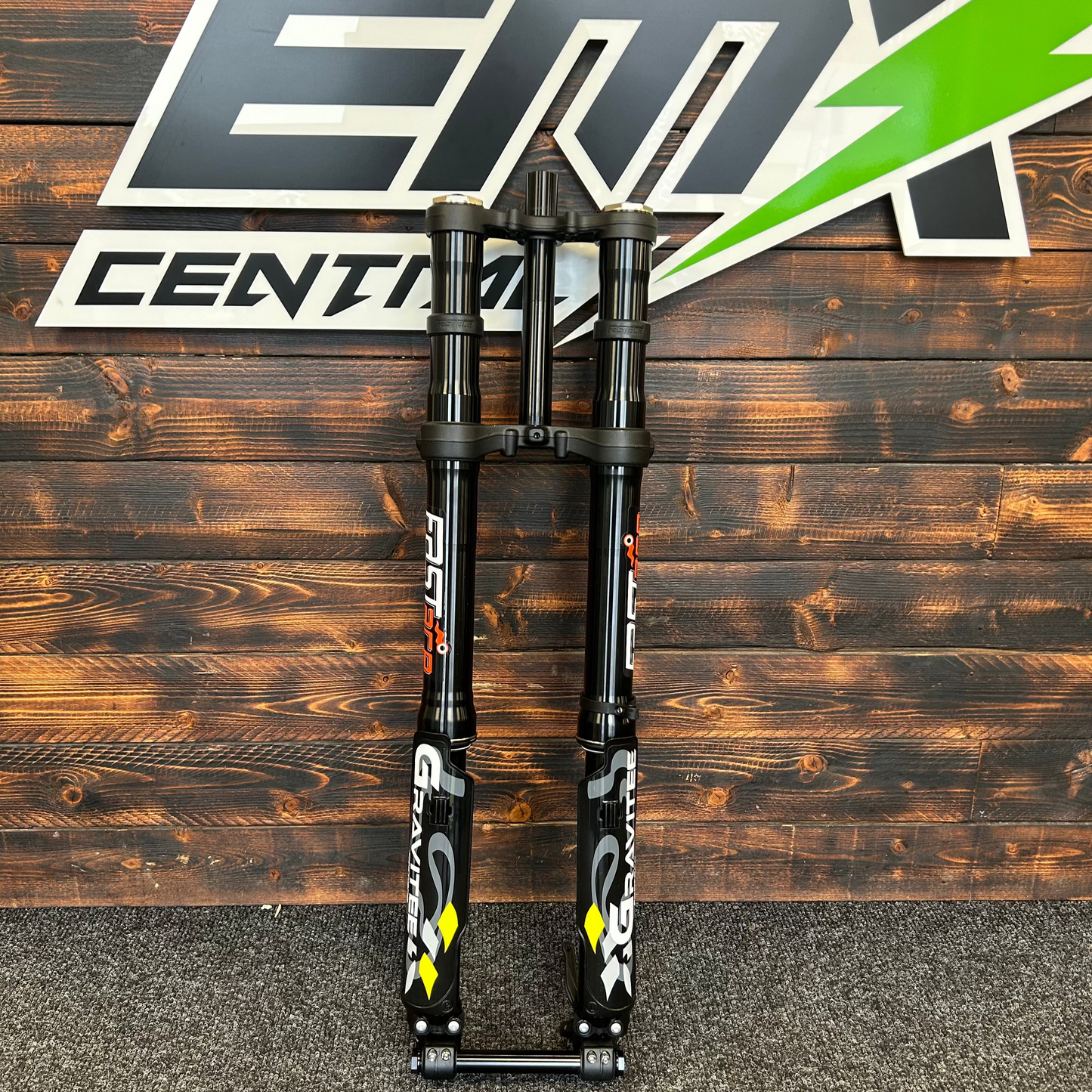 Motorcycle suspension fork on a wooden background with a brand logo.