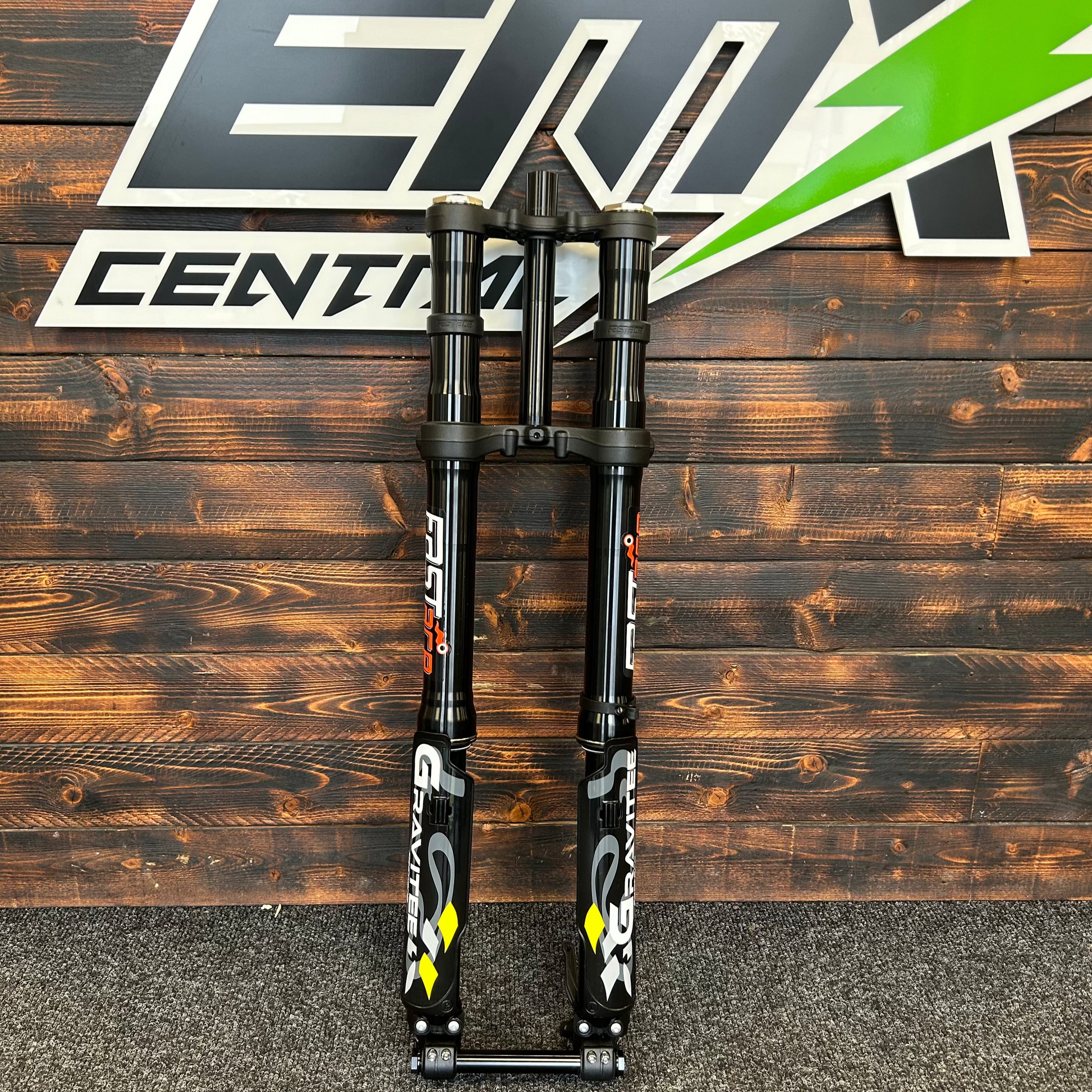 Motorcycle suspension fork on a wooden background with a brand logo.