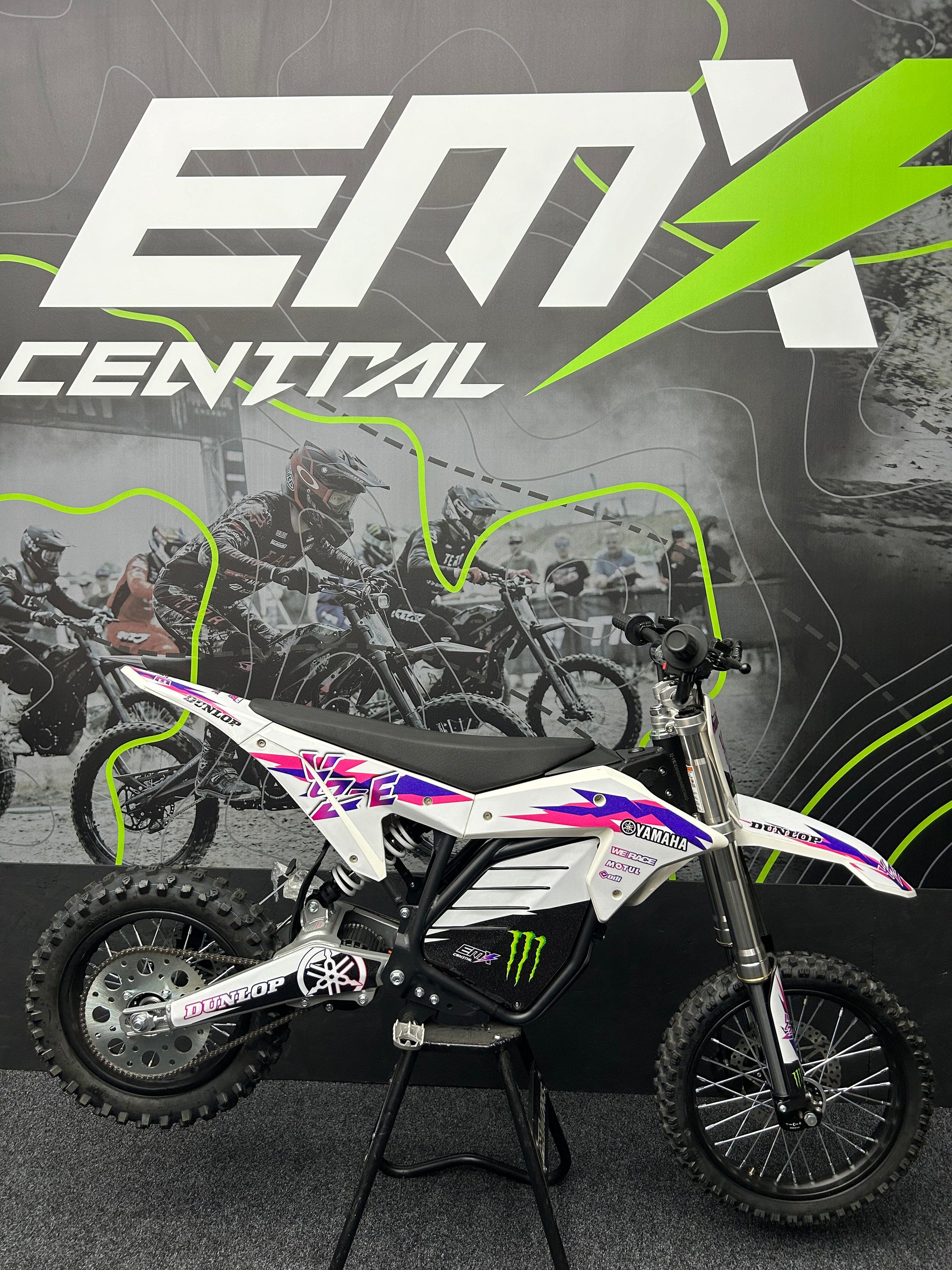 Small dirt bike on a stand with 'EMX Central' branding in the background