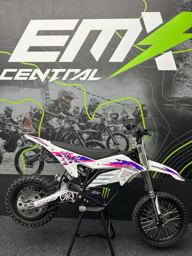 Small dirt bike on a stand with 'EMX Central' branding in the background