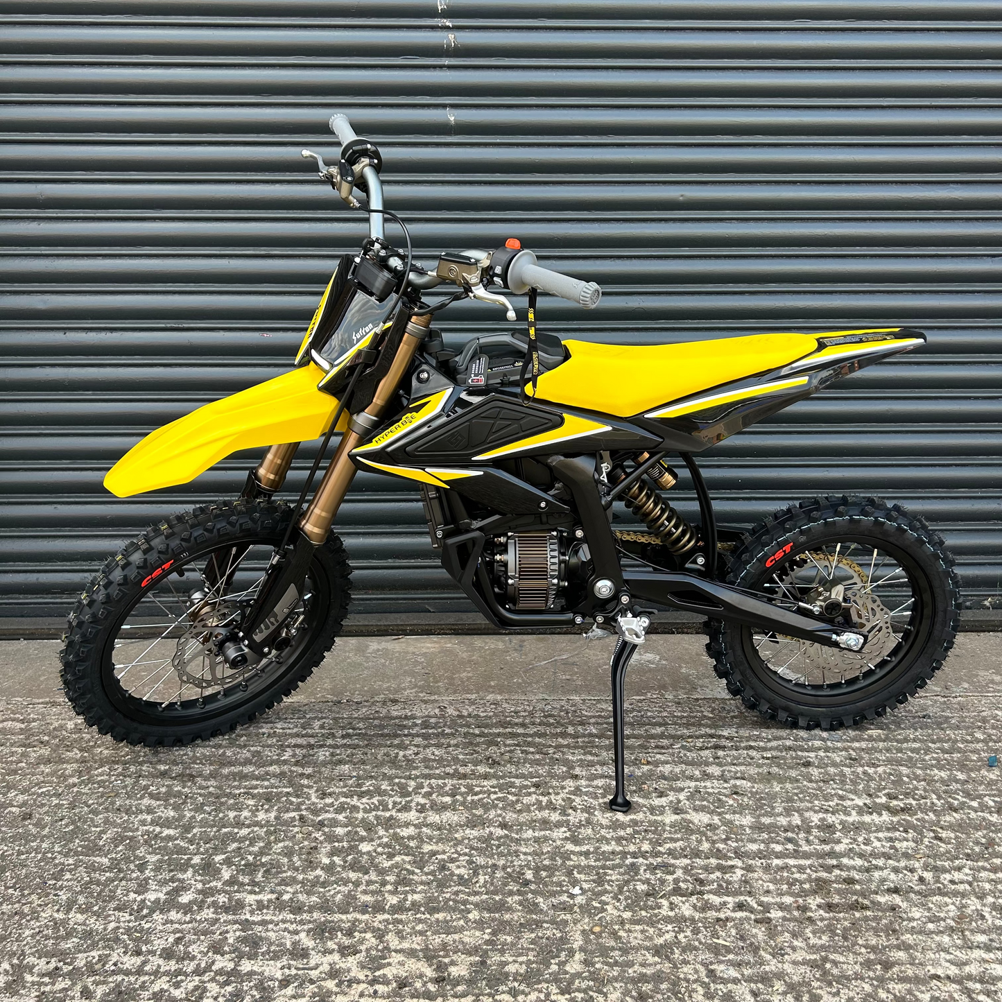 A yellow and black mini dirt bike with a black kickstand, parked on a concrete surface in front of a gray metal garage door.