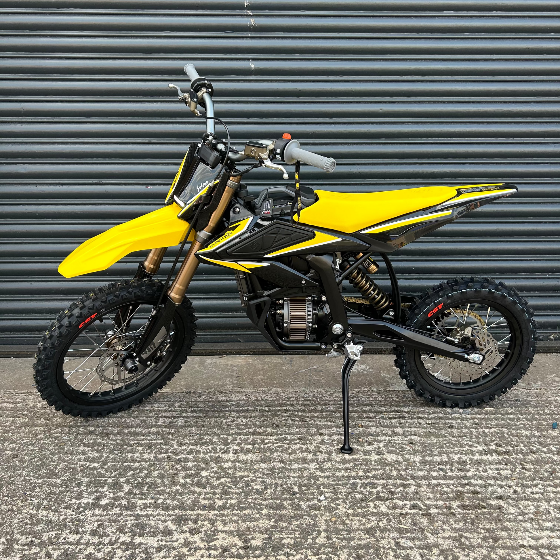 A yellow and black mini dirt bike with a black kickstand, parked on a concrete surface in front of a gray metal garage door.
