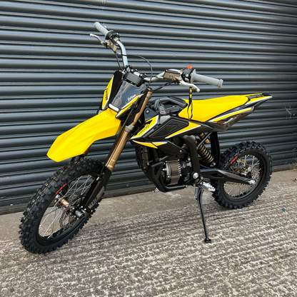 A yellow and black dirt bike with knobby off-road tires, standing on its kickstand in front of a gray metal roll-up door.