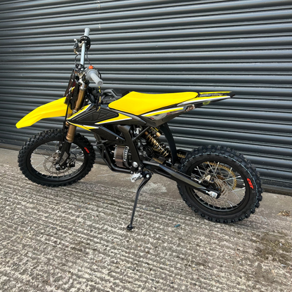 A yellow and black dirt bike with knobby tires, standing on its kickstand in front of a gray metal roll-up garage door.