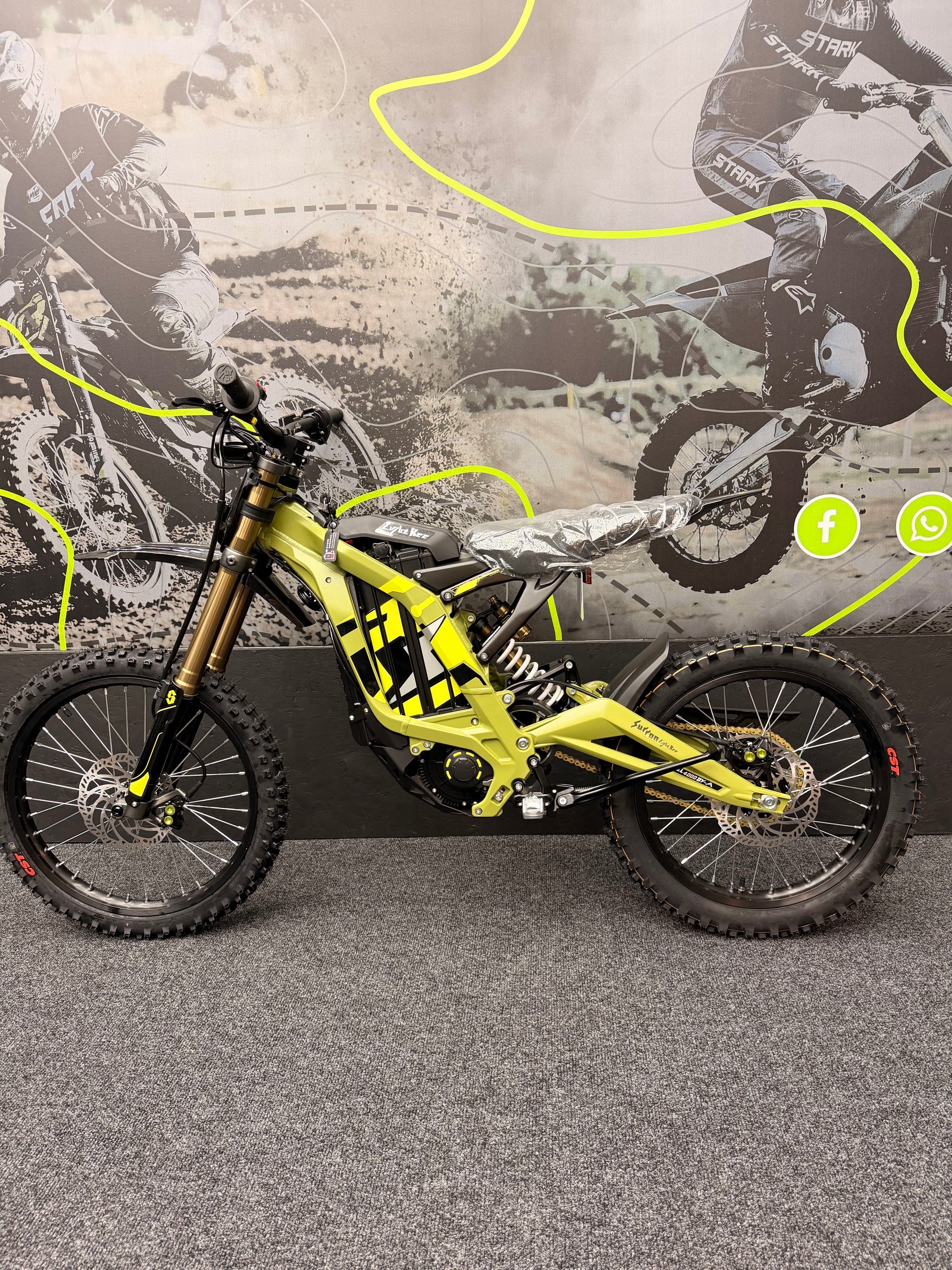 Yellow dirt bike with black tires on a road, with a blurred background of a rider and bike.