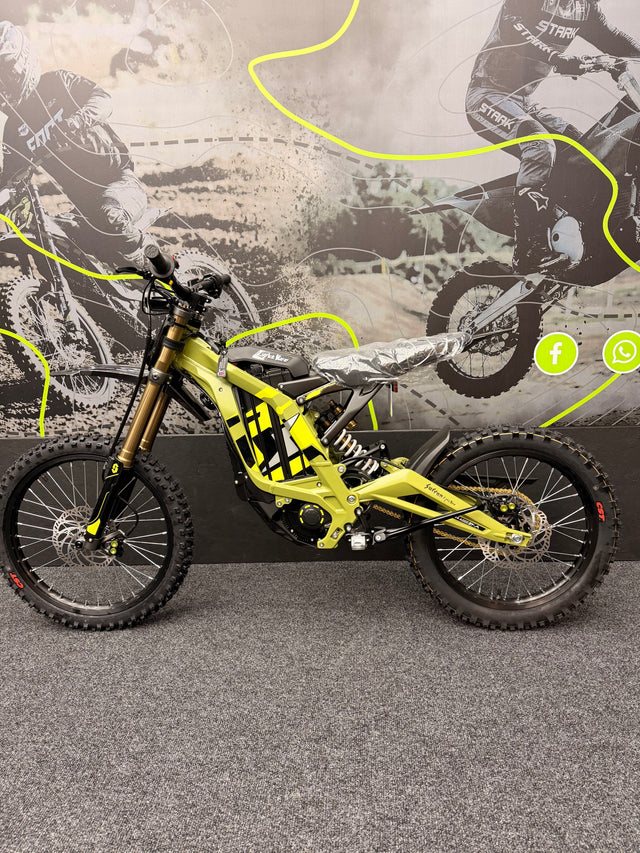 Yellow dirt bike with black tires on a road, with a blurred background of a rider and bike.