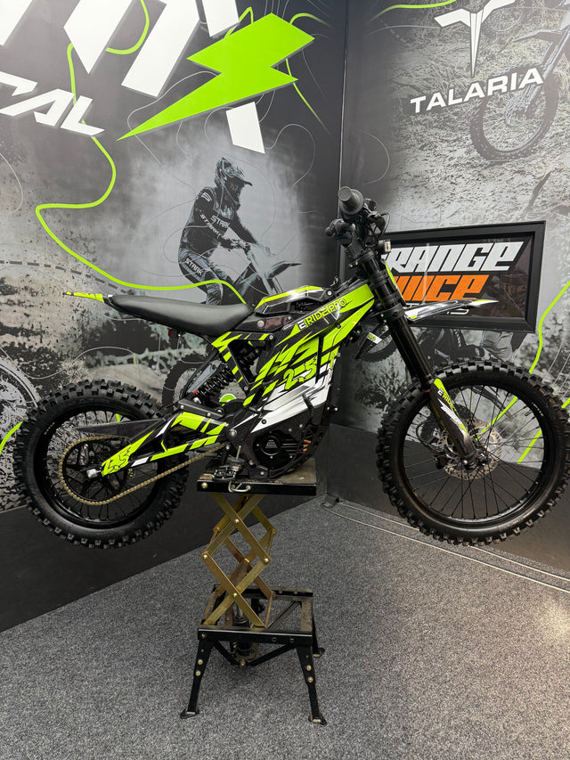 Yellow and black dirt bike on a stand with promotional graphics in the background