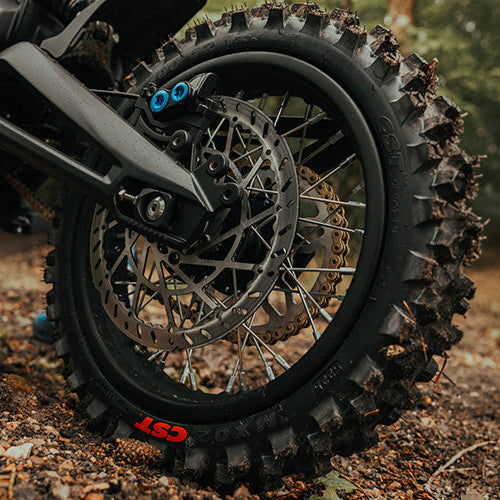 Close-up of a dirt bike tire with knobby tread on a natural ground surface.