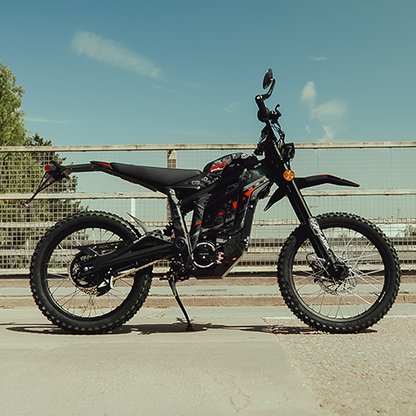 Black electric bike on a road with a metal fence and trees in the background